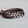 Front view of an adjustable wrap leather bracelet in dark brown, adorned with handmade ribbed sterling silver tubes and finished with a .925 sterling silver lobster clasp. Ideal for minimalists, perfect for wearing alone or stacked. Adjust the knots to fit your wrist.