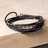 Front view of an adjustable wrap leather bracelet in black, adorned with handmade ribbed sterling silver tubes and finished with a .925 sterling silver lobster clasp. Ideal for minimalists, perfect for wearing alone or stacked. Adjust the knots to fit your wrist.