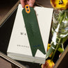 Forest green leather bookmark with blue foil initials, heart, and quote displayed on top of a book