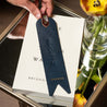 Navy blue custom leather bookmark with name and heart in gold foil and a quote displayed on top of a book