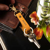 A person holding personalized keychain in mustard leather with brass hardware and gold foil name
