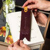 Personalized leather bookmark in eggplant color with custom quote and name displayed on top of a book