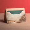 Front view of the Road Tripper personalized leather bifold wallet with a photograph of a red car on a road surrounded by mountains. Perfect for adventure enthusiasts.