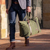 Model carrying an olive waxed canvas duffle bag, perfect for weekend getaways, showcasing premium style and durability.